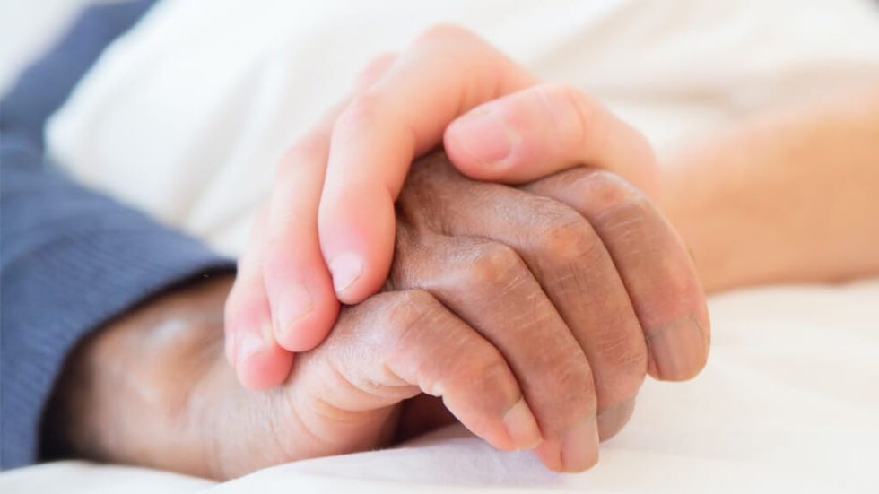 A white hand holding a black persons hand in a hospital bed 1024x576