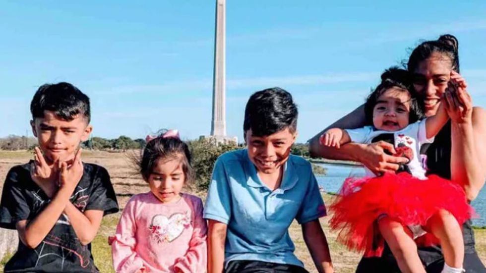 A young family smiling at the camera in front of a large white obilisk and green field