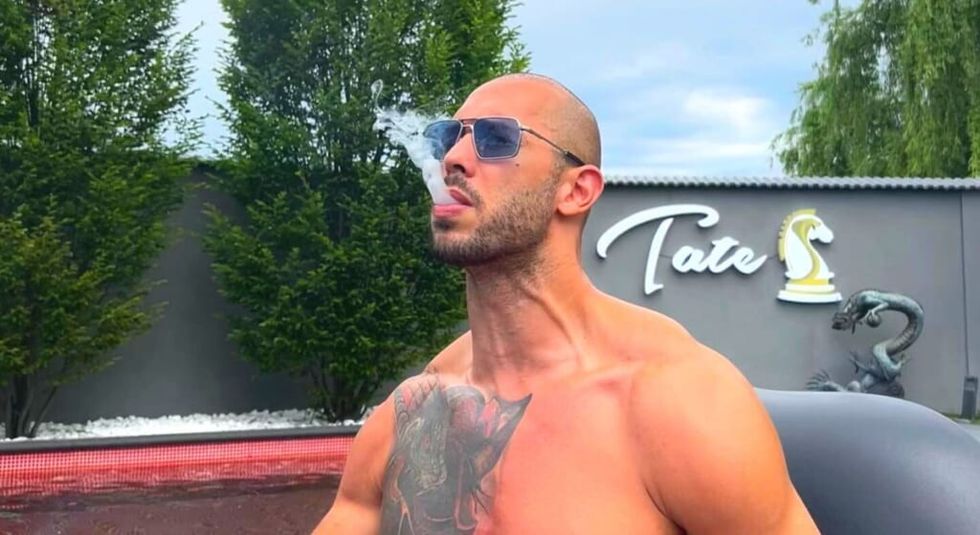 Andrew Tate smoking while showing off chest tattoo.