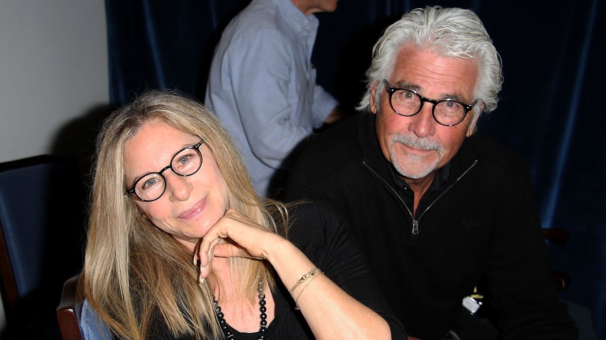 Barbra Streisand in a black outfit and black glasses smiling at the camera next to husbandand James Brolin.