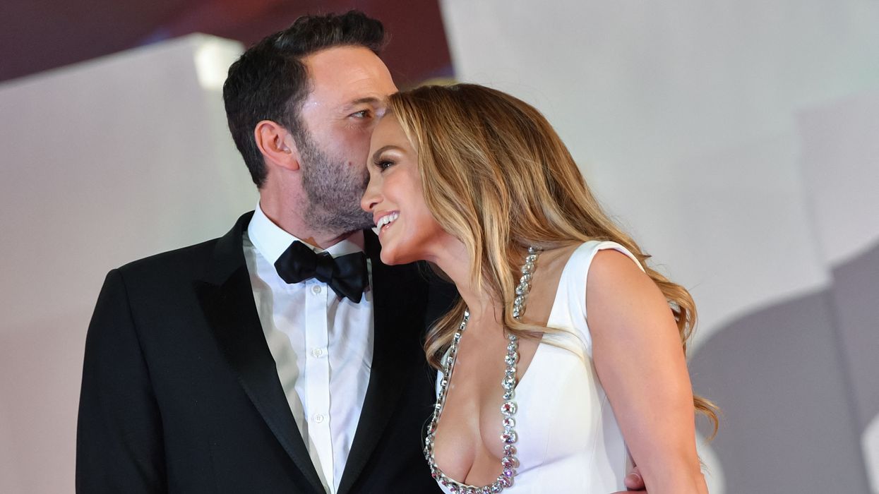 Ben Affleck in tux kissing the top of wife Jennifer Lopez who is radiant in a white dress. 