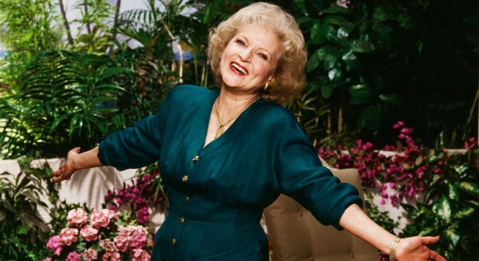 Betty White in green dress, arms spread out in the Golden Girls backyard