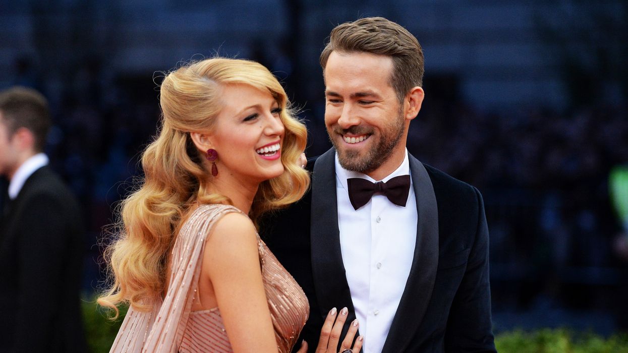 Blake Lively in pink champagne dress posing next to her husband Ryan Reynolds on the red carpet.