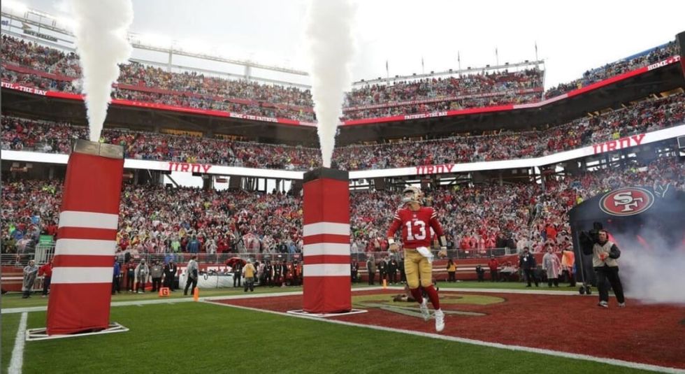 Brock Purdy running onto the field in red 49ers jersey.