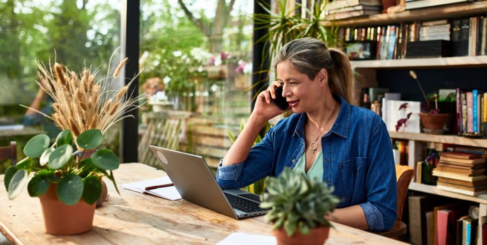 Businesswoman using mobile phone in front of laptop