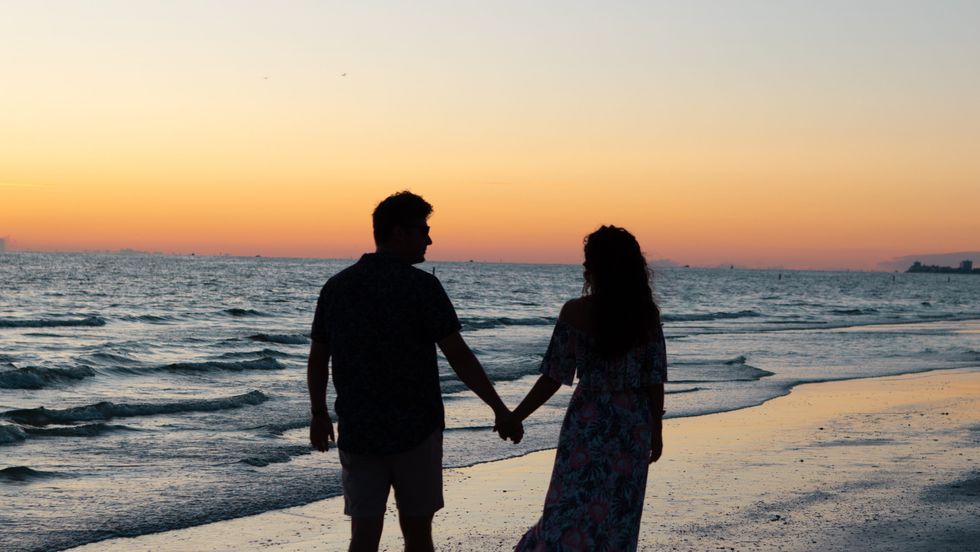couple holding hands and walking on the beach at sunset