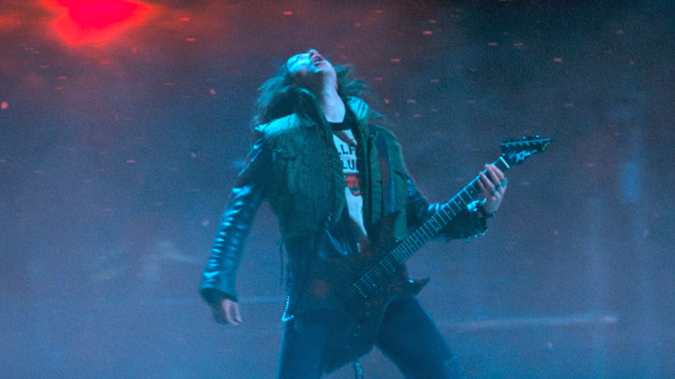 Eddie Munson playing guitar with a dark blue backdrop in the Upside Down.