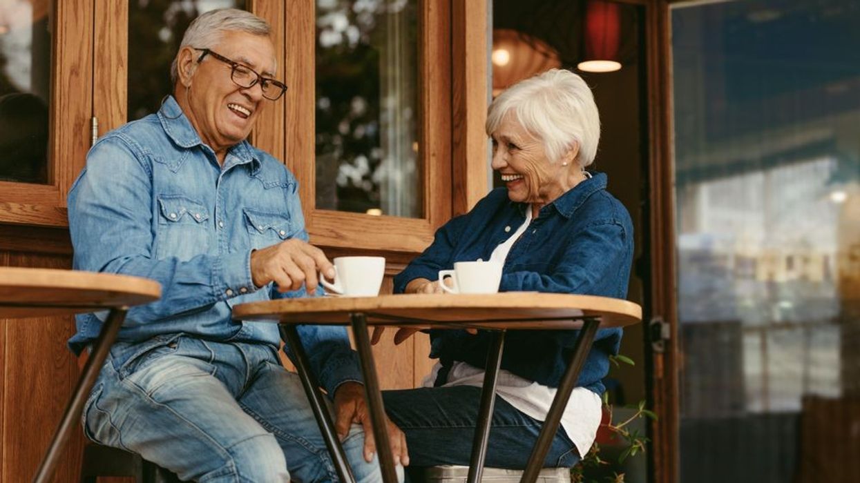 elderly couple laughing and drinking coffee outside a restaurant