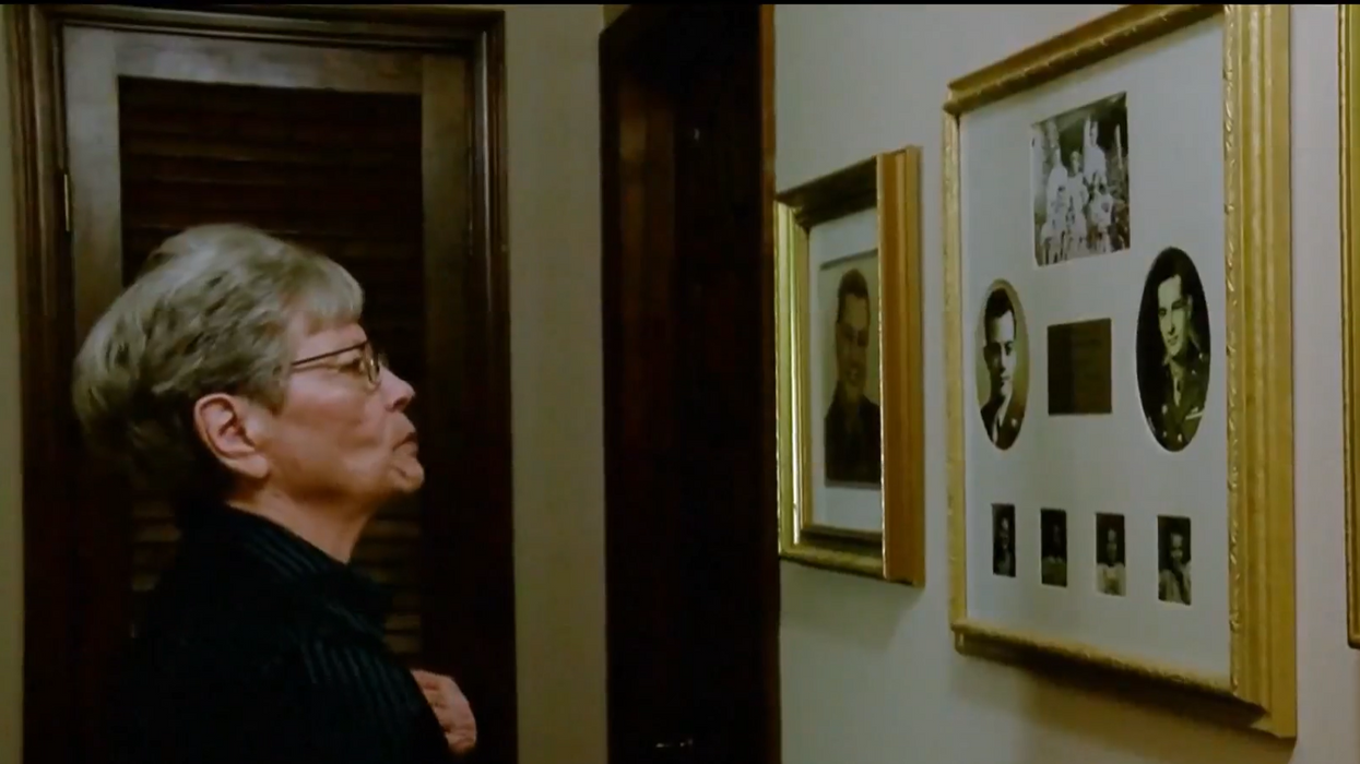 Elderly woman looking at framed pictures on the wall.