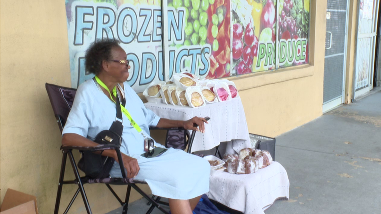 Elderly woman sells baked goods outside.