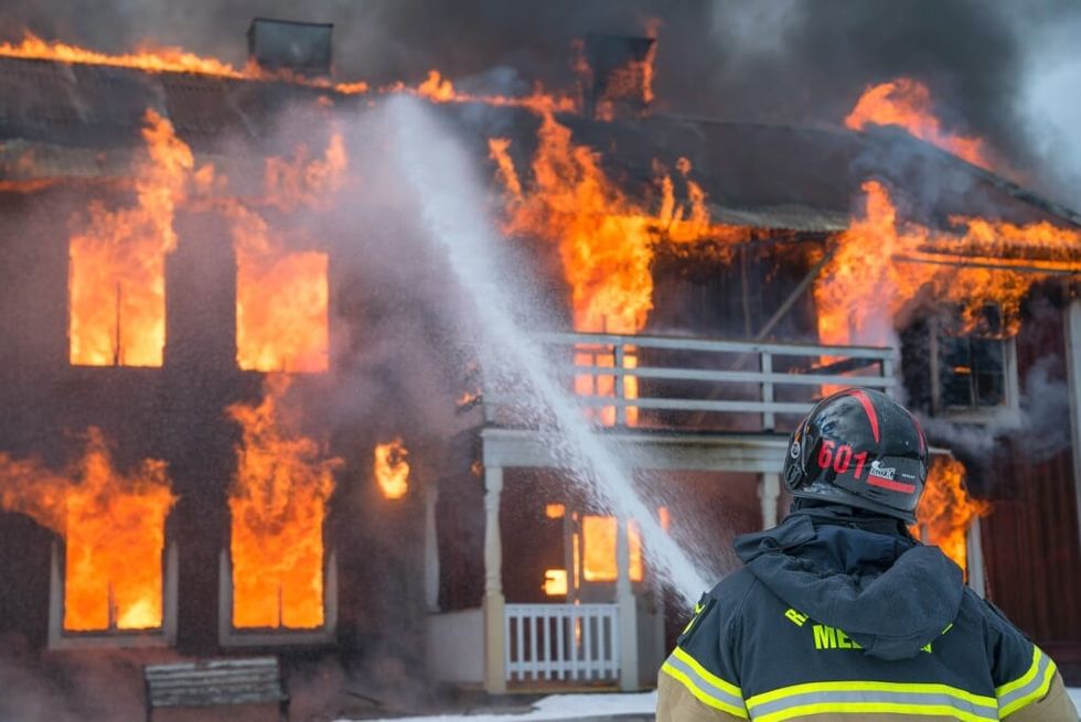 firefighter spraying water on burning house