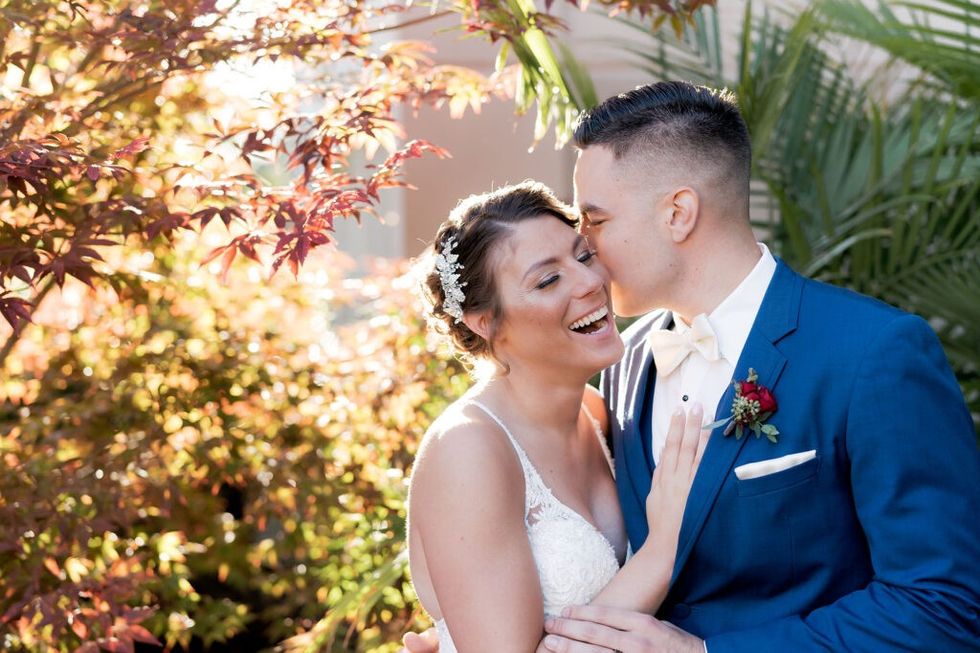 Groom kisses bride on cheek in garden