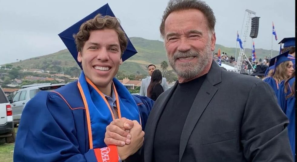 Joseph Baena wearing graduate cap and gown shaking his dad, Arnold Schwarzenegger's hand.