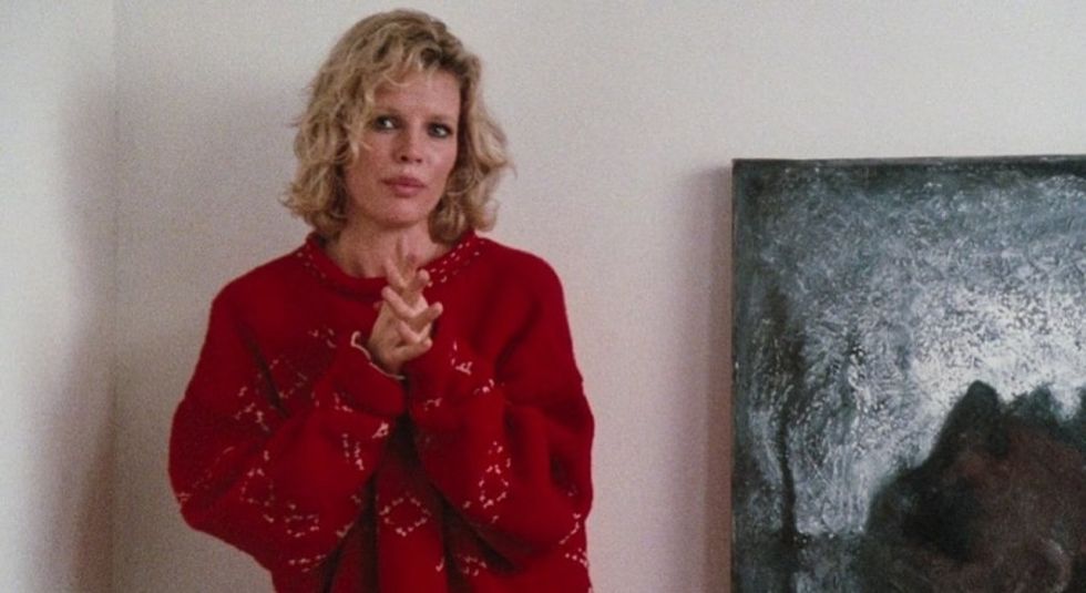 Kim Basinger in red sweater with hands together.