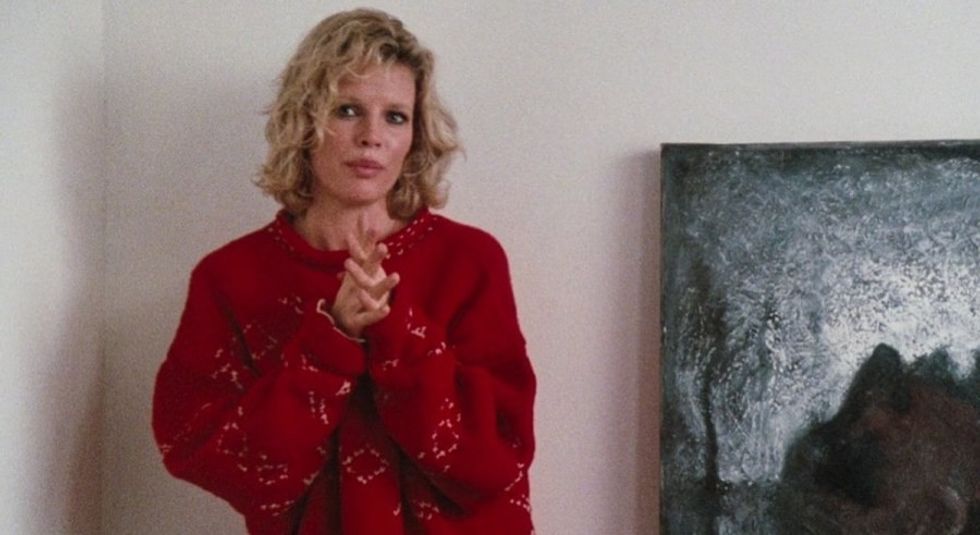 Kim Basinger in red sweater with hands together.
