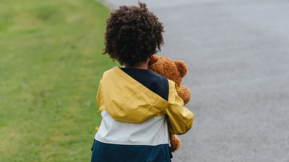 little boy holding a stuffed toy and walking on the street alone