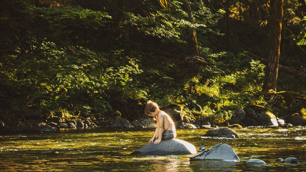 little boy sitting on a rock near the river