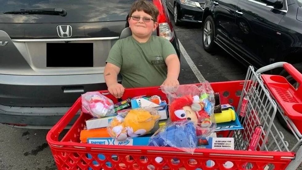 little boy standing with shopping cart filled with toys