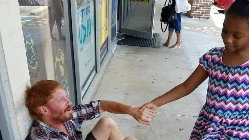 little girl holding a man's hand. Man sitting on the ground.