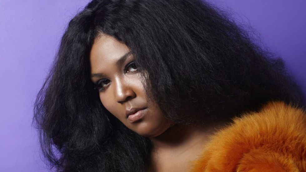 Lizzo wearing an orange fur coat against a purple background