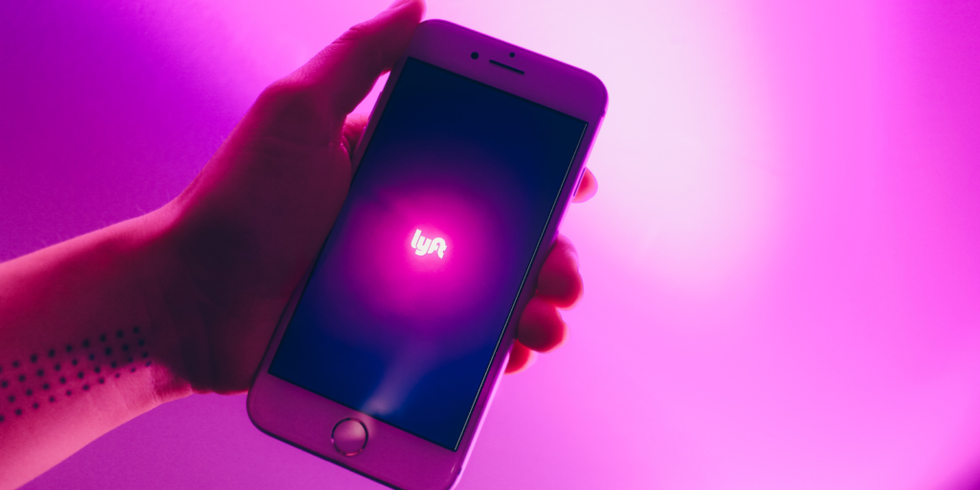 lyft logo on phone in front of a bright purple-pink background