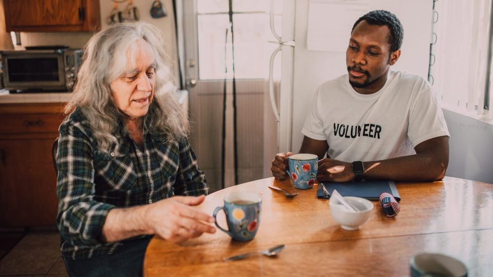 man and elderly woman drinking from mugs sitting at dining table