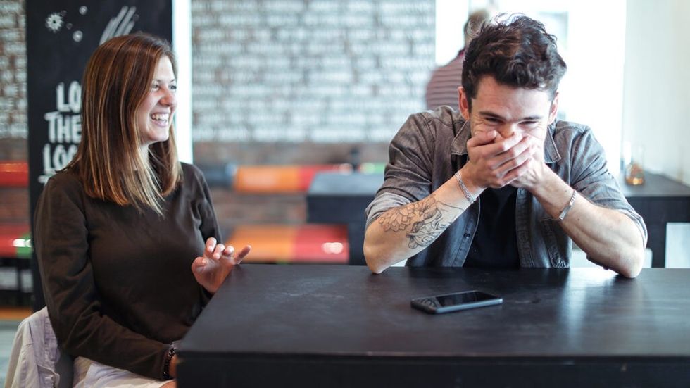 Man and woman laughing, seated at table together