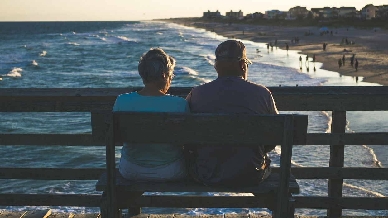 Man and woman sitting on a bench and facing a beach