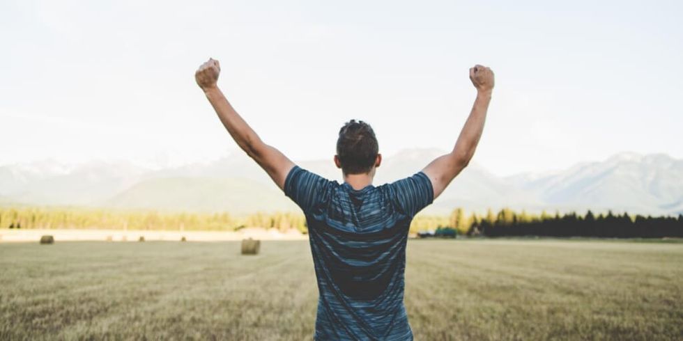 Man looking out at field with arms raised victoriously by Japheth Mast on Unsplash