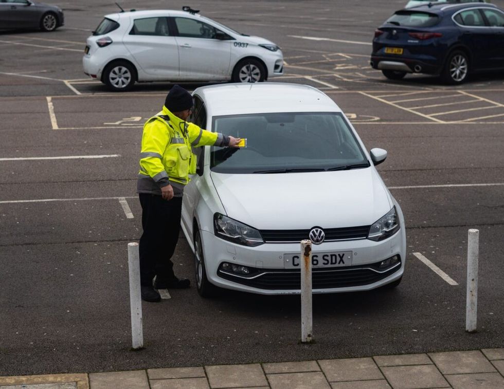 man placing a parking ticket on a car windshield