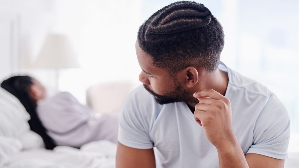 man sitting on bed, looking over at woman sleeping