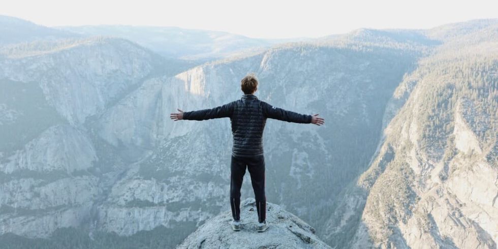Man standing atop a mountain with arms wide open overlooking mountains by Jason Hogan on Unsplash