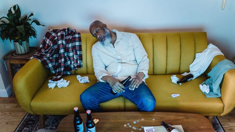 man wearing a white tshirt asleep on a messy couch
