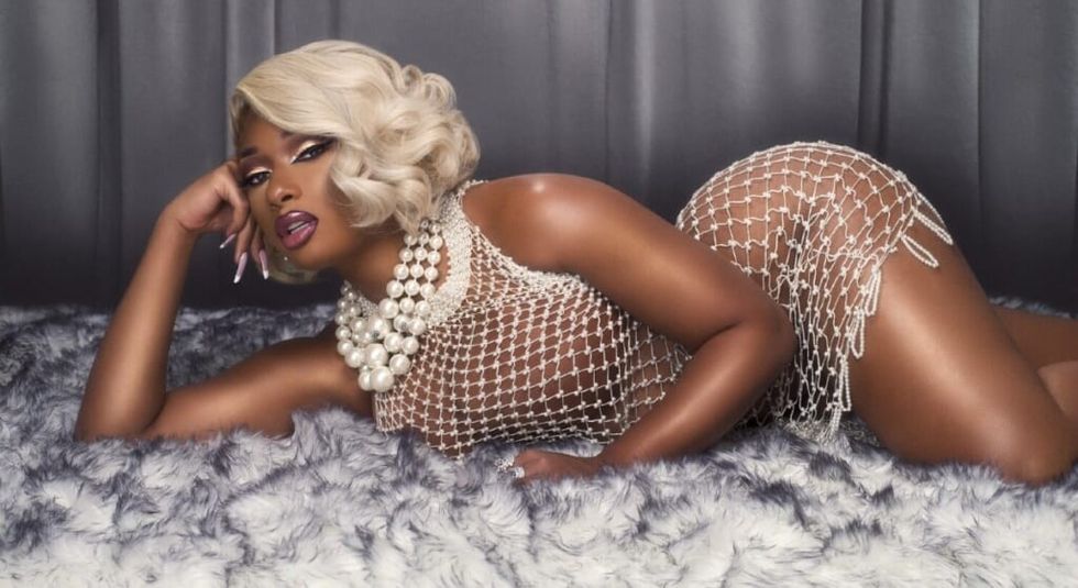 Megan Thee Stallion in dress and blonde hair laying on a carpet.
