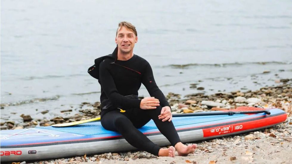 Mike Shoreman in a wetsuit on his board on the banks of a lake