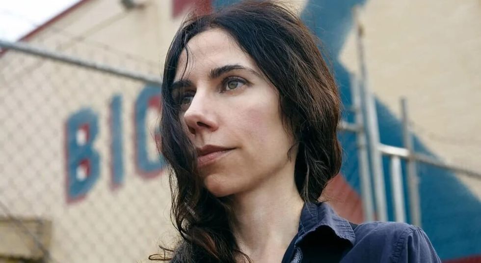 Musician PJ Harvery outside in front of a chain link fence