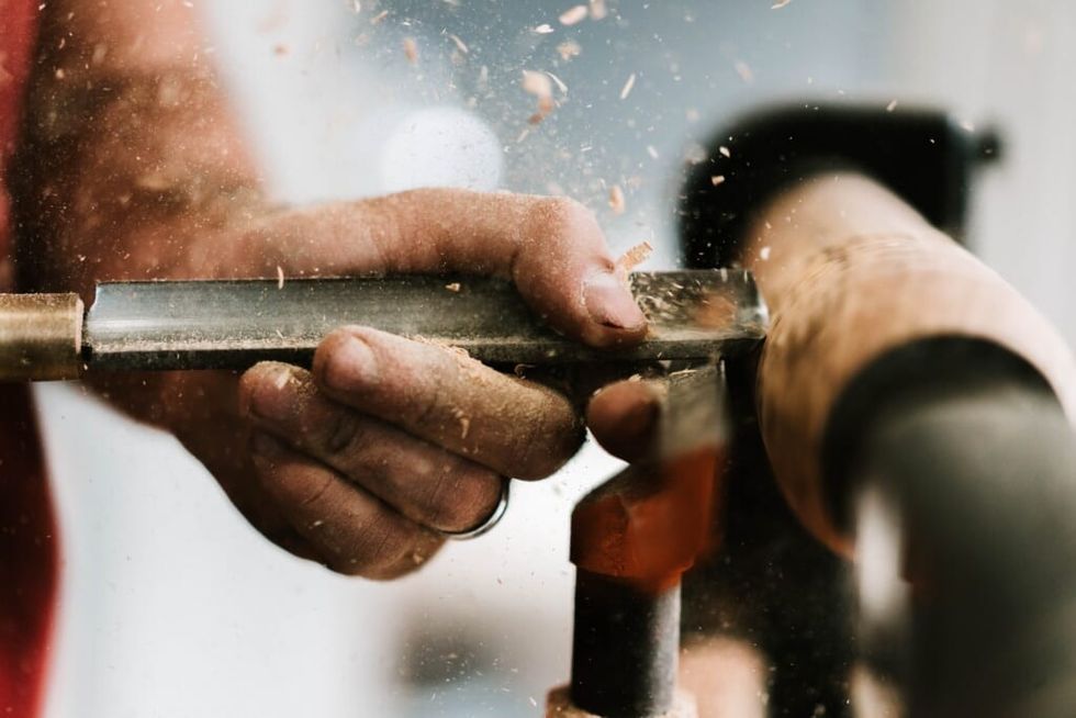person holding silver and orange pipe, working on wood