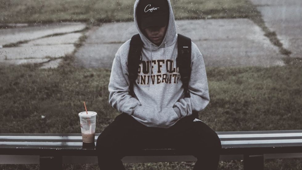 person sitting on a bench in a hoodie and cap