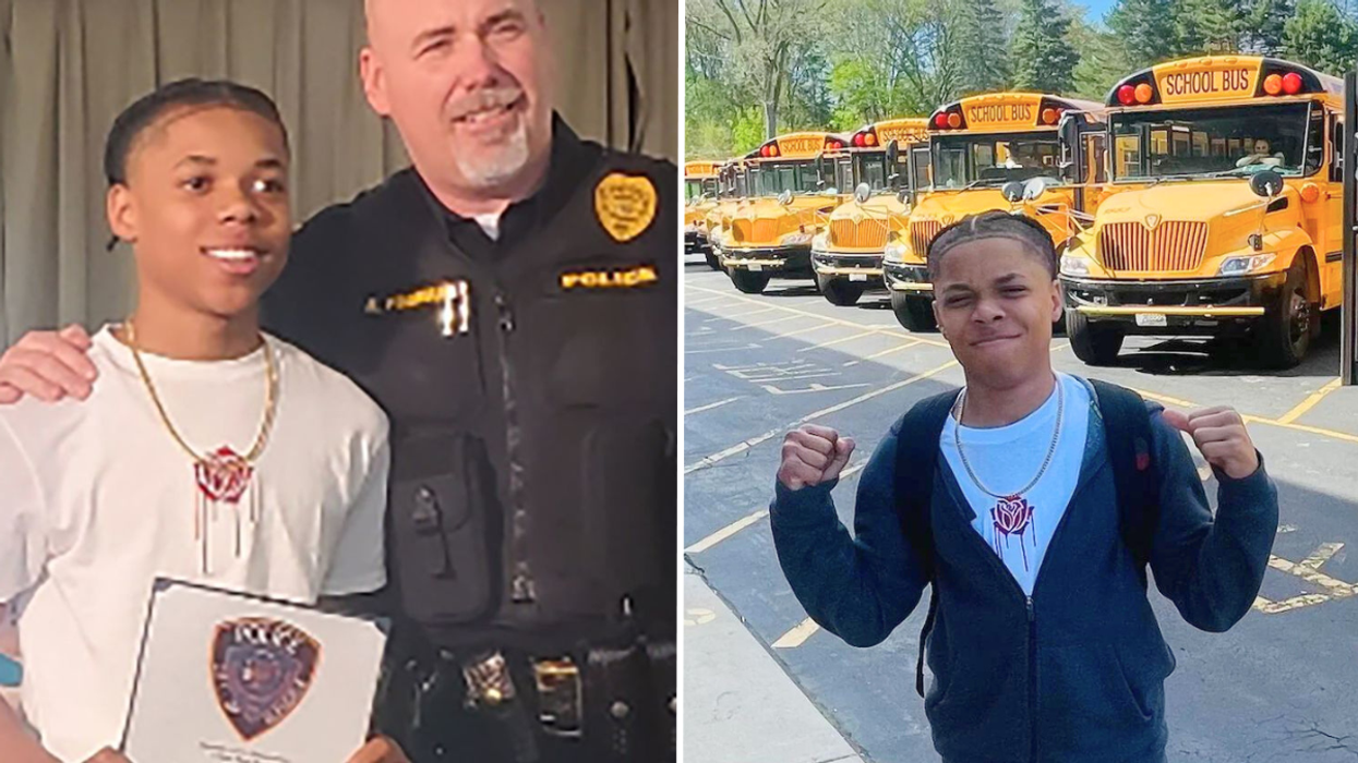 Police officer standing next to a teenager and a teen standing in front of a row of school buses.