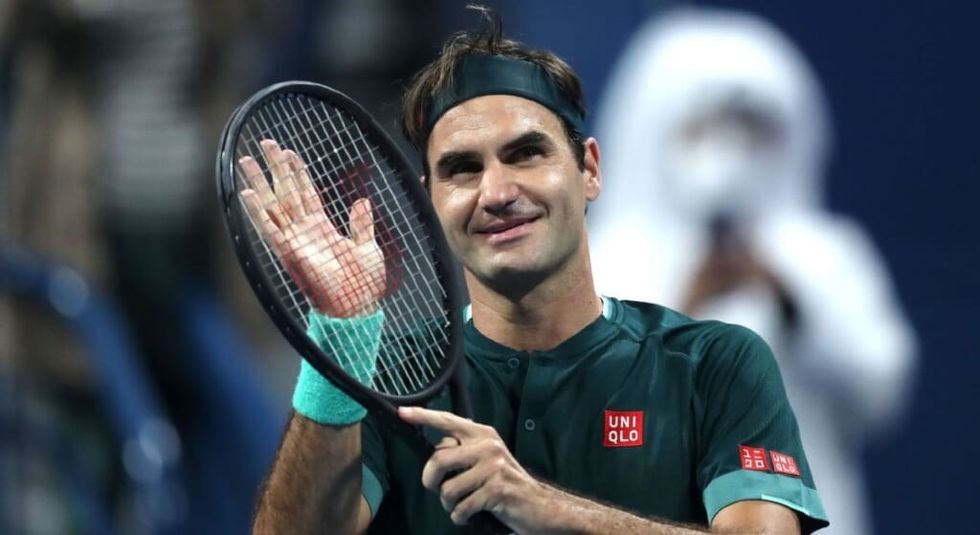 Roger Federer in black jersey smiling and touching his racket.