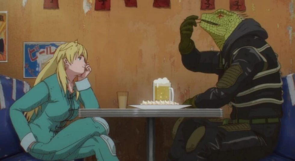 Screenshot from Dorohedoro of Nikaido and Caiman sitting at a restaurant table. Nikaido is wearing blue coveralls and looking fondly at Caiman while Caiman is devouring his favourite food, gyozas.