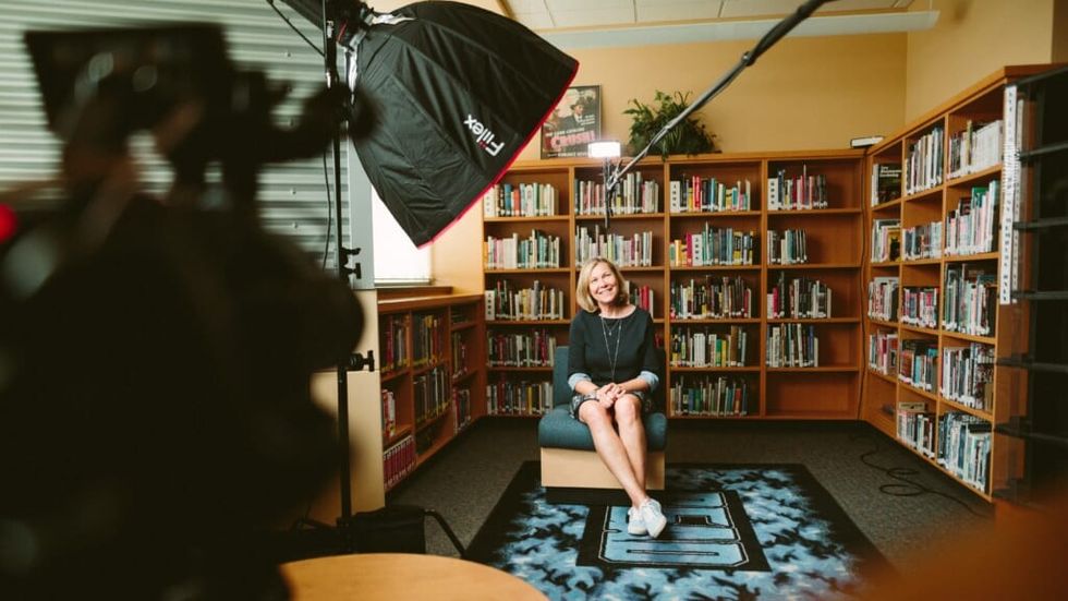 smiling woman sitting in a chair in front of shelves full of books