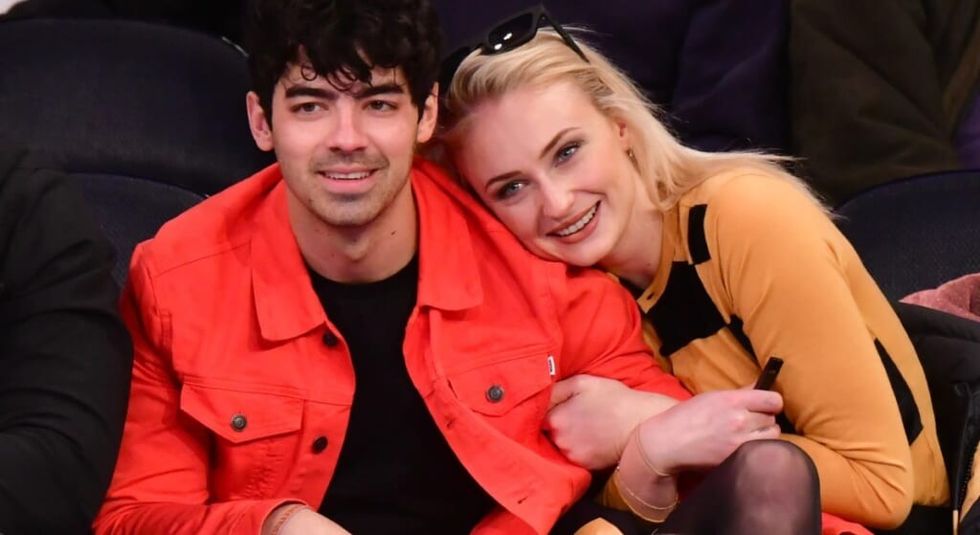 Sophie Turner in orange shirt hugging husband Joe Jonas.