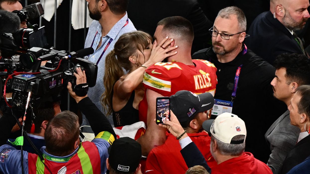 Taylor Swift and Travis Kelce kissing passionately at the Superbowl while surrounded by journalists and cameramen. 