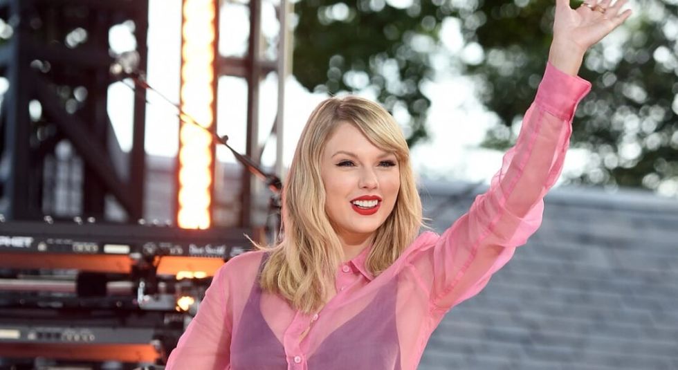 Taylor Swift dressed in pink smiling and waving to fans.
