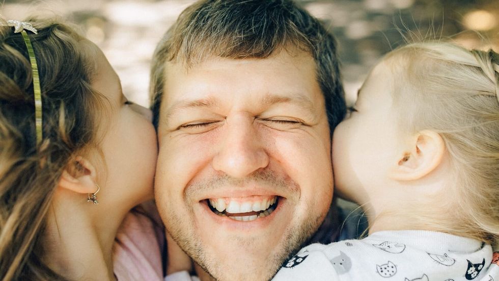 two little girls kissing their father on the cheek