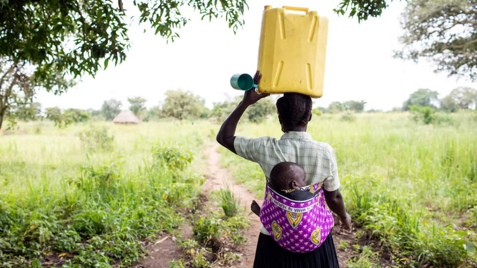 woman carrying a baby on her back and holding a yellow container on her head