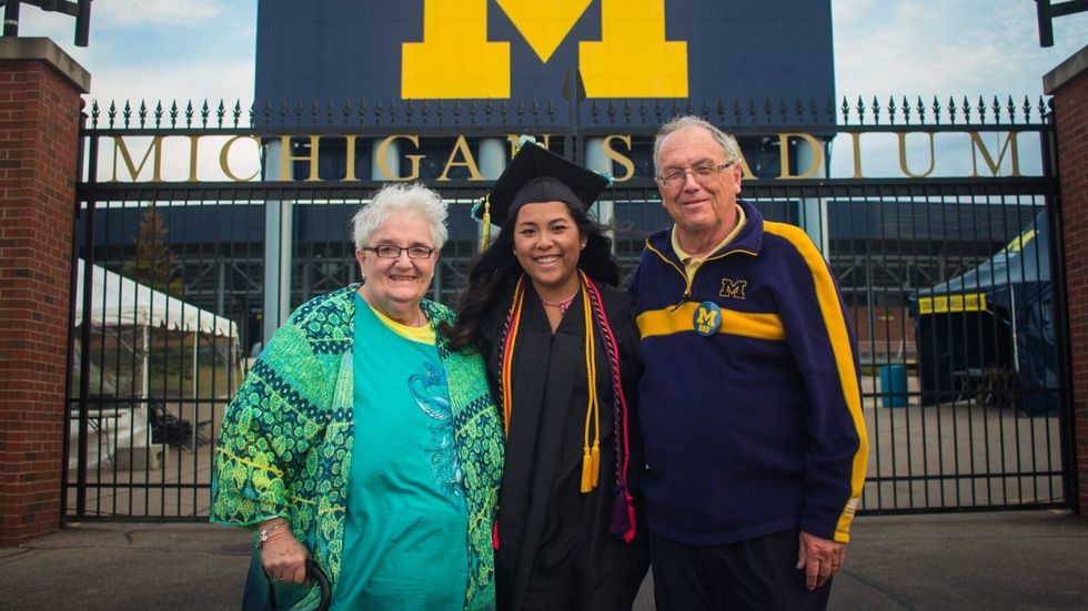 woman in a graduation gown with a man and a woman on either side.