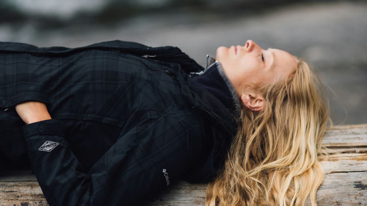 Woman in black zip-up jacket leaning on large log at daytime