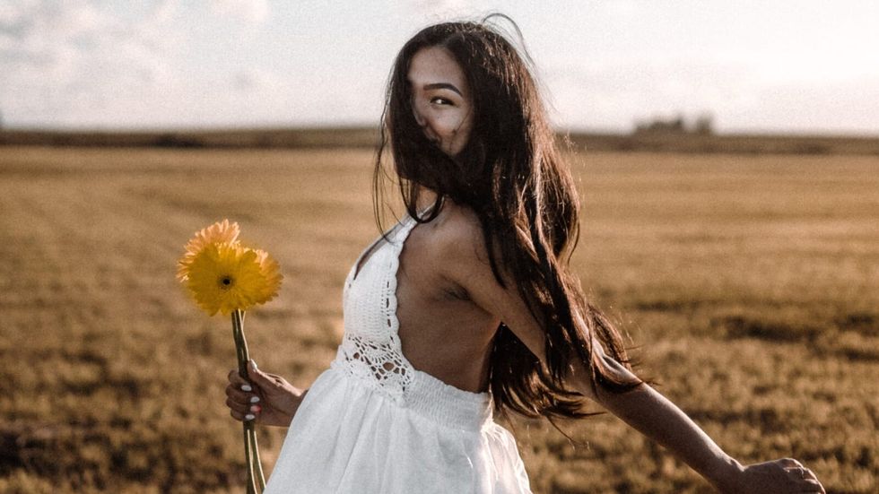 woman running in a field wearing a white dress and holding a flower